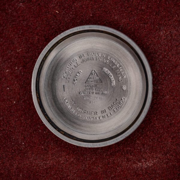 A gold capped Omega Automatic Seamaster Ref. 2846-2848 "Deluxe" case back with engraved text, shown on a red textured surface.