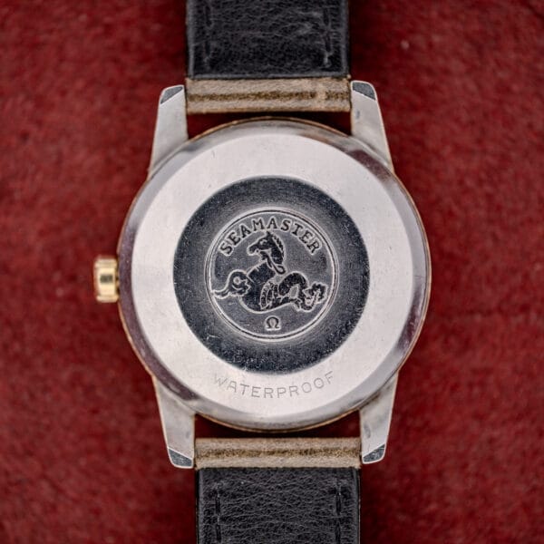 Close-up of the back of an Omega Automatic Seamaster Ref. 2846-2848 "Deluxe" gold capped case, featuring waterproof engraving against a red textured background.