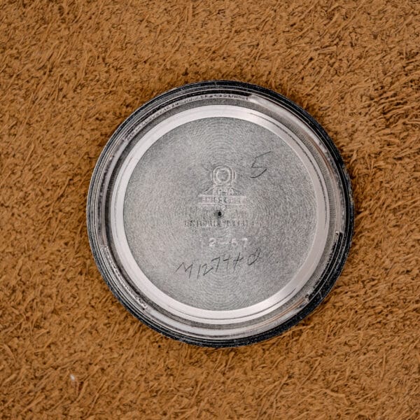 A 1967 Enicar Seapearl 600 Sherpa Ref. 100/120 Cal. 1010 stainless steel case back, with engraved and handwritten markings, rests on a brown textured surface.