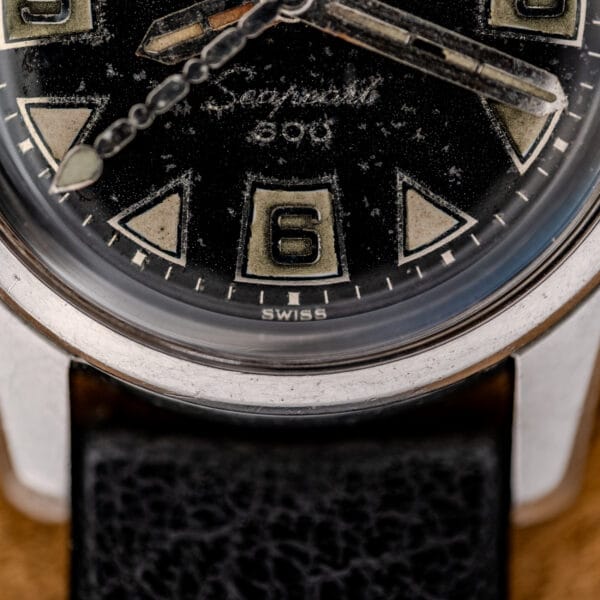 Close-up of a 1967 Enicar Seapearl 600 Sherpa Ref. 100/120 Cal. 1010 watch face, showing the number 6, bold hands, and "SWISS" at the bottom on its stainless steel case.