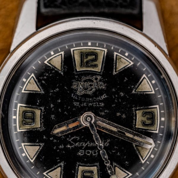 Close-up of a 1967 Enicar Seapearl 600 Sherpa Ref. 100/120 wristwatch, featuring Cal. 1010 movement, large numbers, worn black dial, and stainless steel details.