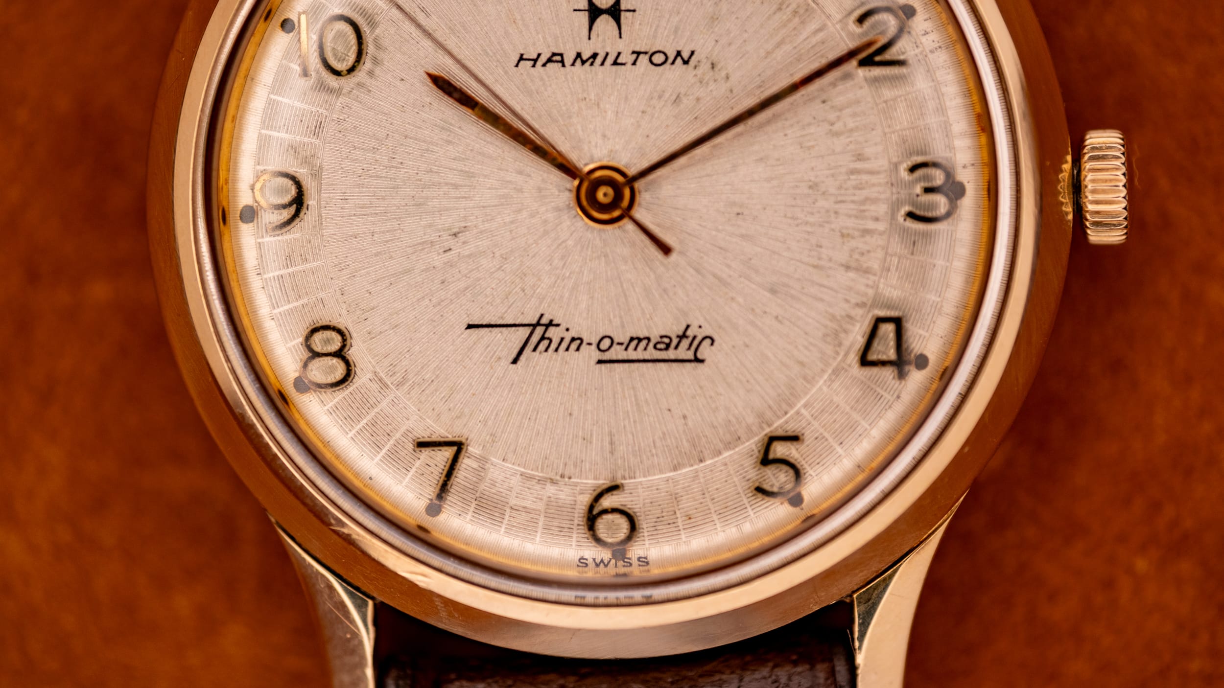 Close-up of a vintage Hamilton Thin-o-matic wristwatch with gold-toned case and brown leather strap, showcasing the classic style of the Hamilton collection.