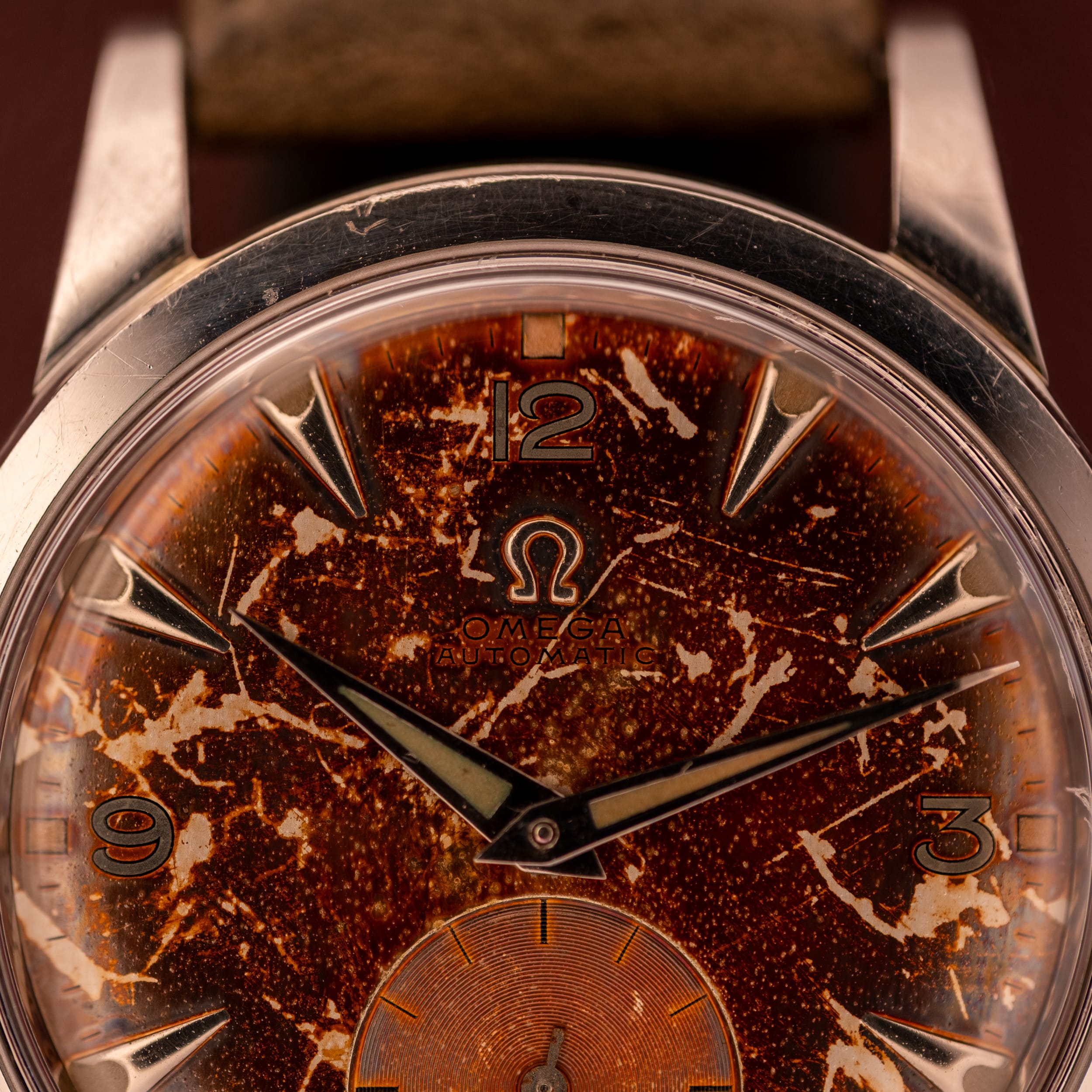 Close-up of a vintage Omega wristwatch featuring a tropical brown, heavily patinated dial and silver hour markers.