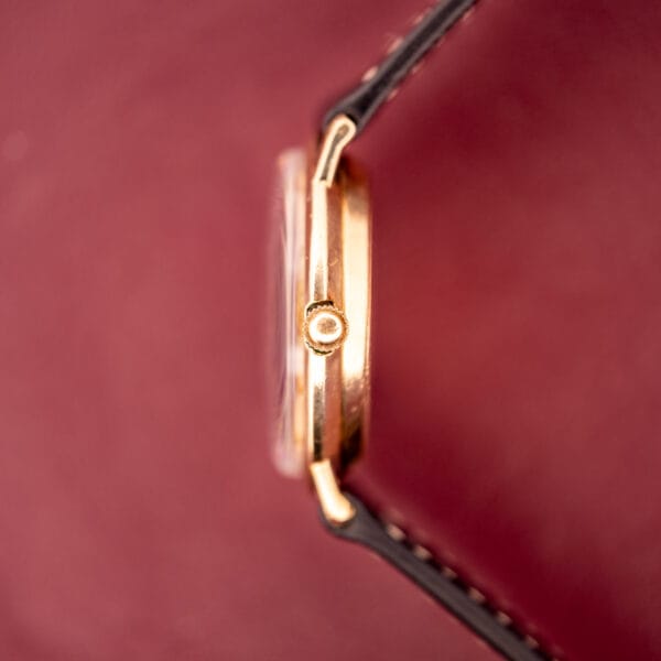 Side view of a Hamilton Thin-O-Matic 10k Gold Filled Case Automatic wristwatch with a black leather strap, displayed against a vibrant red background.