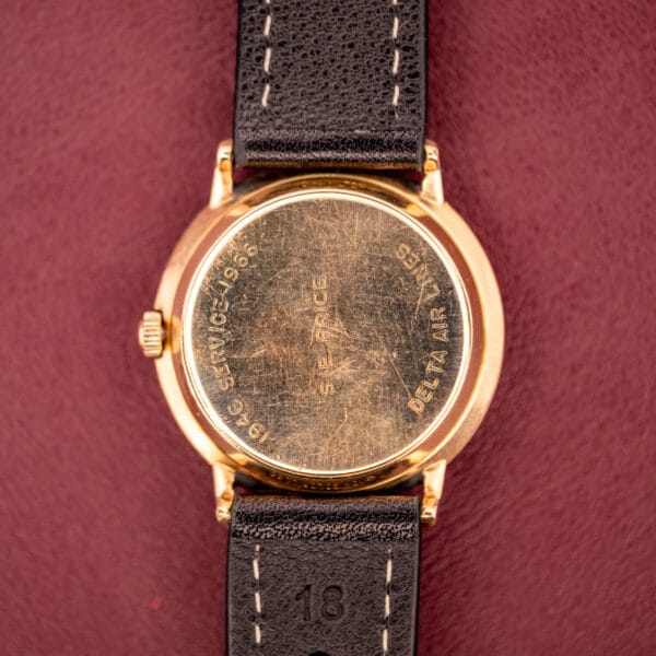 Hamilton Thin-O-Matic 10k Gold Filled Case Automatic watch with back engraved "1966 SERVICE DELTA AIR LINES," gold filled case, black leather strap, displayed on a maroon surface.
