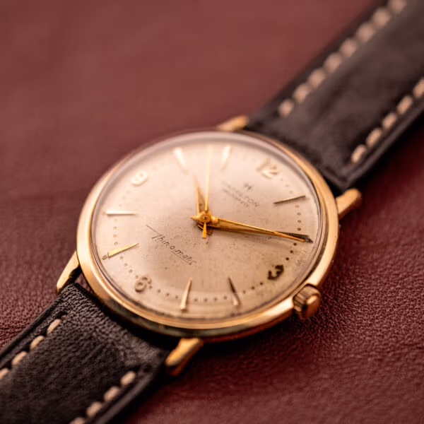 Hamilton Thin-O-Matic 10k gold filled case three-quarter view on burgundy leather, factory cream dial with gold dauphine hands.