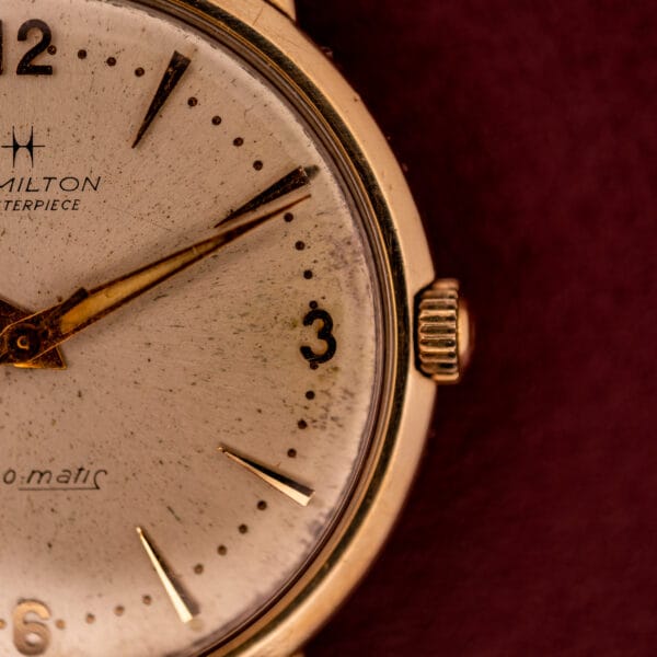Close-up of a Hamilton Thin-O-Matic 10k Gold Filled Case Automatic wristwatch, displaying 2:13 on its dial against a maroon background.