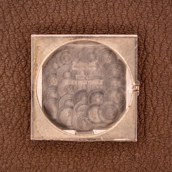 The Zodiac Ref. 523-007 Square Case Manual Wind Cal. 52 features an engraved silver back and classic design details, displayed on a textured brown surface, highlighting its distinctive manual wind movement.