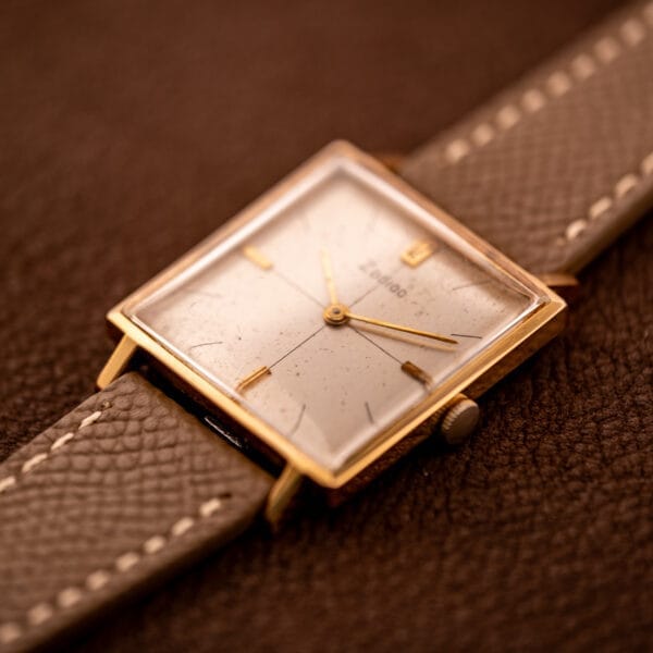 A Zodiac Ref. 523-007 square case wristwatch with manual wind Cal. 52 movement and leather strap, shown on a textured brown surface.