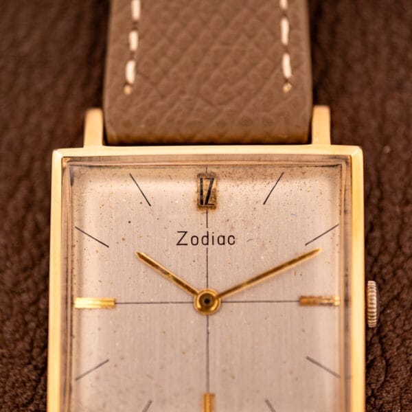 Close-up of a Zodiac Ref. 523-007 Square Case Manual Wind Cal. 52 wristwatch with a brown leather strap, displayed on a textured surface.