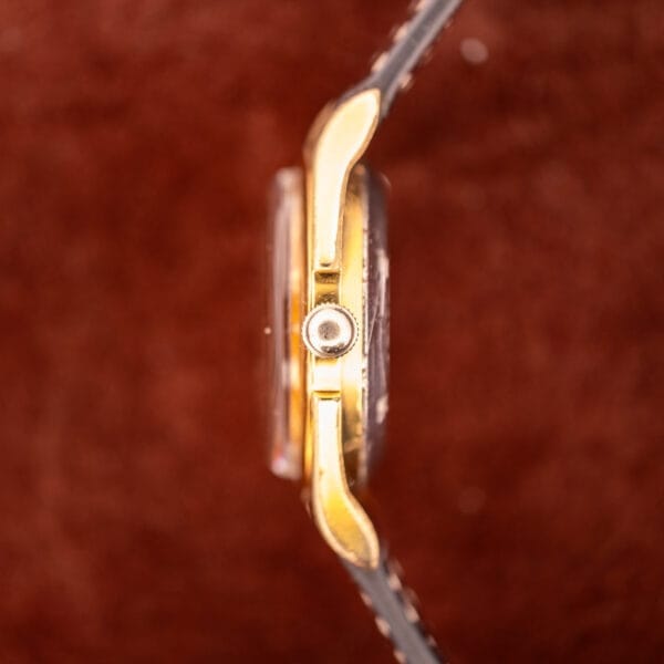 Side view of a gold Zodiac Rotographic Ref. 656 Tropic Dial Automatic Cal. 1381 wristwatch with a black leather strap, set against a blurred brown background.