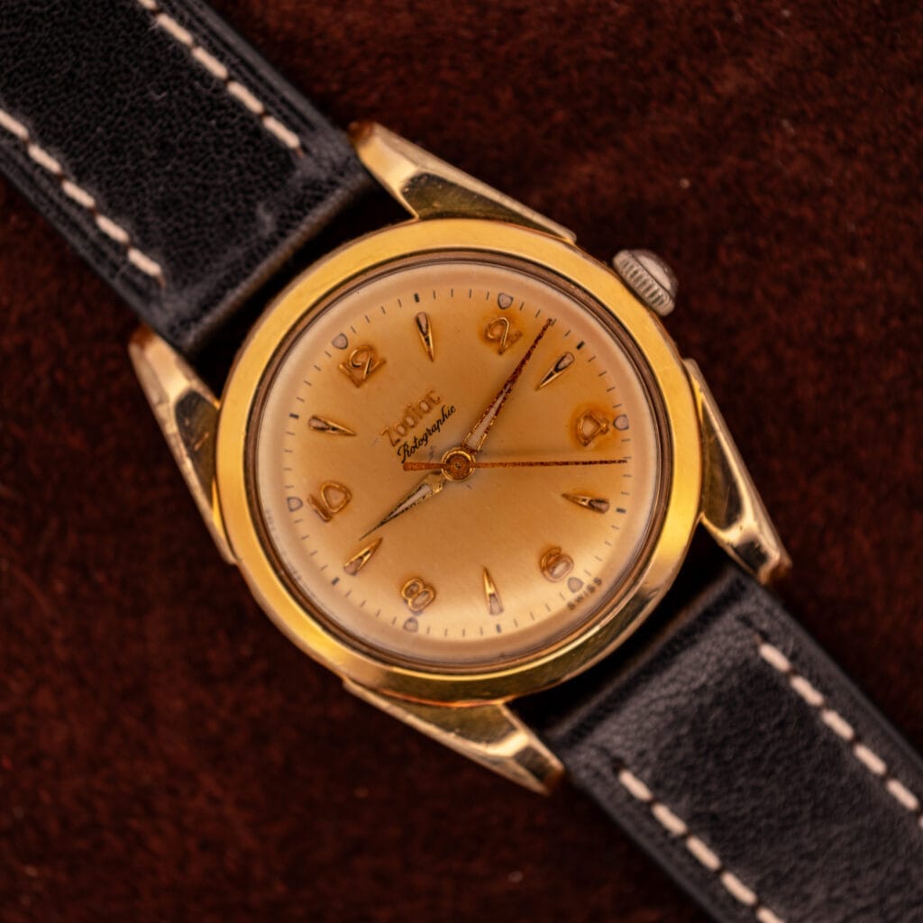 A vintage Zodiac Rotographic Ref. 656 with a Tropic Dial, automatic Cal. 1381, gold case, and black leather strap is set against a dark brown background.