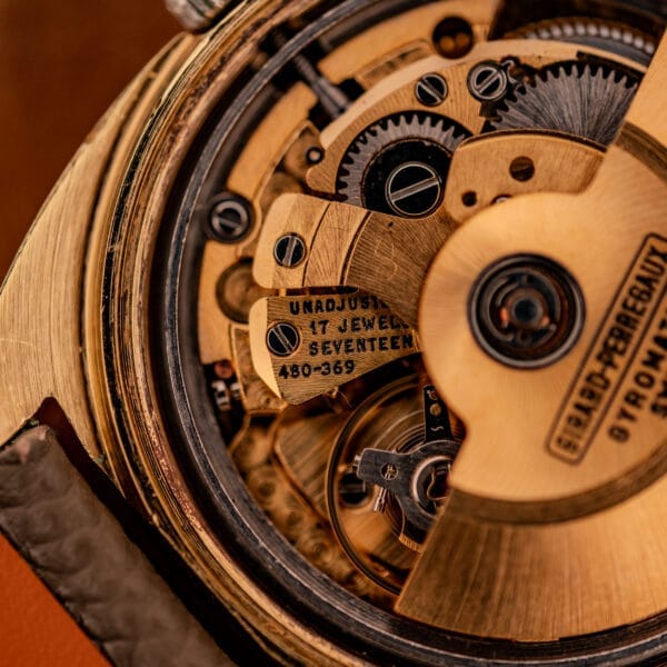 Close detail of the Girard Perregaux 480-369 caliber showing UNADJUSTED, 17 JEWELS, and 480-369 stamped into the bridge alongside the balance wheel.