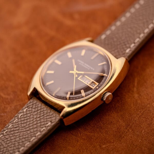 Angled photograph of the GP Gyromatic 9276 HA, brown dial catching shadow and the cushion case profile visible against a tan leather background.