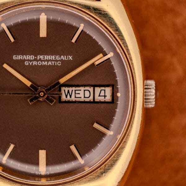 Close detail of the GP Gyromatic dial with ribbed gold baton markers, day/date aperture at three, and signed crown visible at the case side.