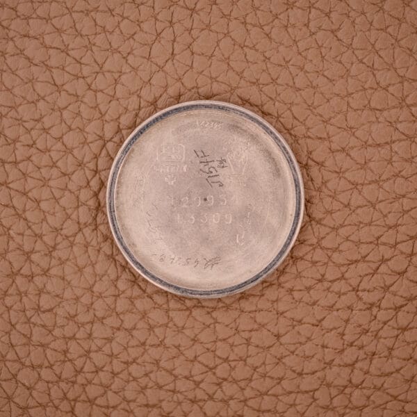 The Movado Manual Wind Sub-Seconds 14K Rose Gold Cap Ref. 13309 features an engraved case back resting on brown textured leather, showcasing its refined craftsmanship and sector dial design.