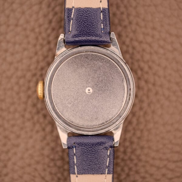 The Movado Manual Wind Sub-Seconds 14K Rose Gold Cap Sector Dial Ref. 13309, featuring a sector dial, blue leather strap, and gold crown, is displayed on a textured brown surface.