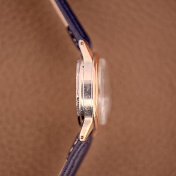 Side view of the Movado Manual Wind Sub-Seconds 14K Rose Gold Cap Sector Dial Ref. 13309, featuring a blue leather strap, set against a textured brown background.