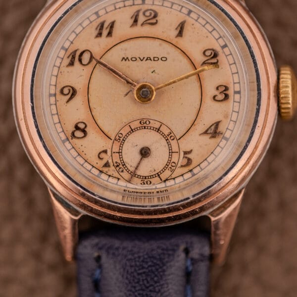 Close-up of a Movado Manual Wind Sub-Seconds 14K Rose Gold Cap Ref. 13309 wristwatch, featuring a sector dial, black numerals, and a blue leather strap.