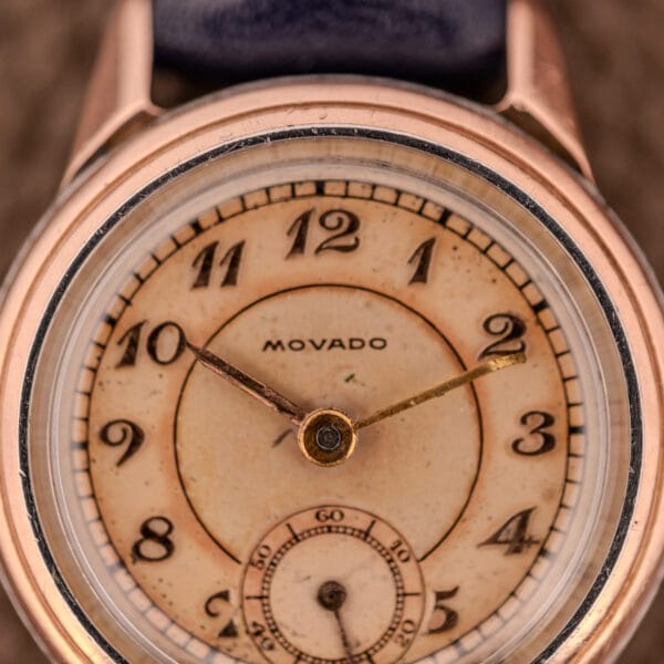 Close-up of a Movado Manual Wind Sub-Seconds 14K Rose Gold Cap Sector Dial Ref. 13309 wristwatch, featuring black numbers, manual wind movement, and visible wear on the dial.