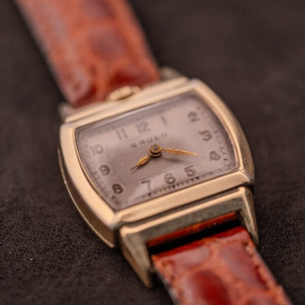 A vintage Gruen "Top Crown" 10K Gold Filled 17 Jewels Ref. 400-298 wristwatch from the 1940s with a square case and brown leather strap, displayed on a dark surface.