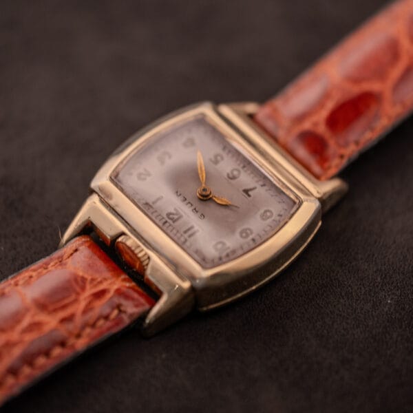 A Gruen "Top Crown" 10K Gold Filled 17 Jewels Ref. 400-298 c.1940s wristwatch with a square case and brown leather strap, displayed on a dark background.