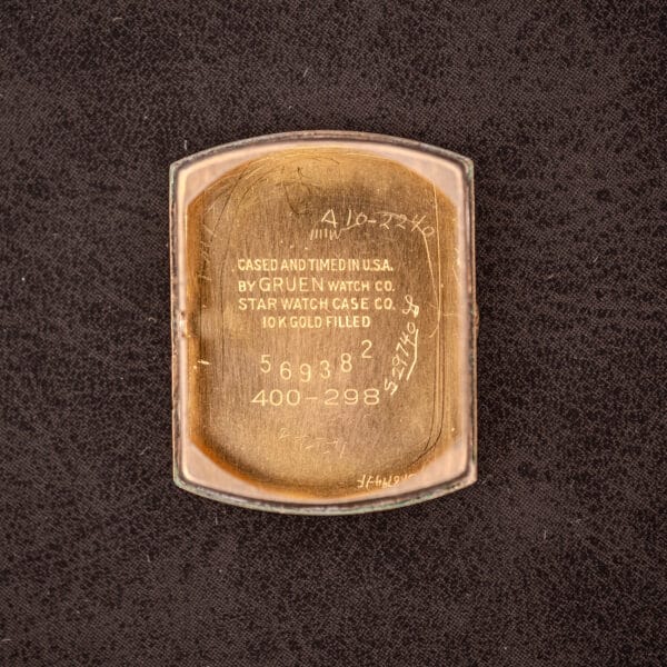 Back of a Gruen "Top Crown" 10K Gold Filled 17 Jewels Ref. 400-298 c.1940s watch case with engraved serial numbers and markings, shown on a dark textured background.