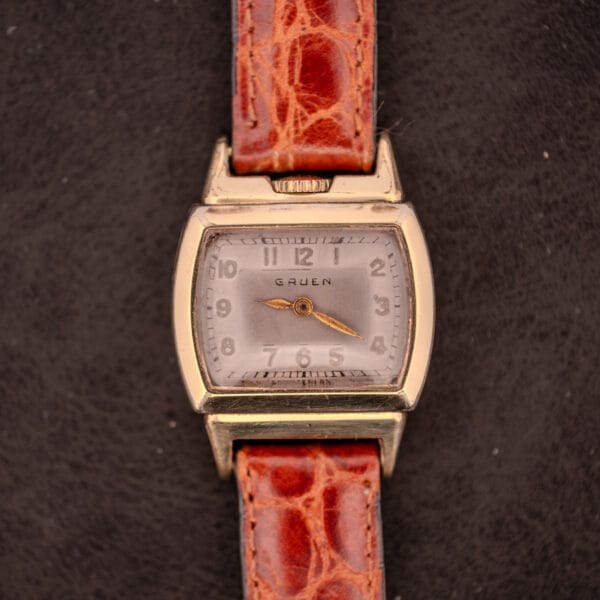 A vintage Gruen "Top Crown" 10K Gold Filled 17 Jewels Ref. 400-298 c.1940s wristwatch with a brown leather strap rests on a dark surface.