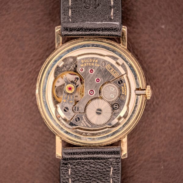 Close-up of a Bulova Manual Wind Date 10K RGP Cal. 11ALD c.1968 watch with its back removed, displaying the intricate gears and movement.