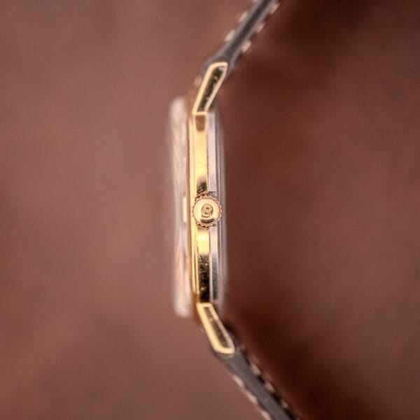 Side view of a Bulova Manual Wind Date 10K RGP Cal. 11ALD c.1968 wristwatch with a brown leather strap, set against a blurred brown background.