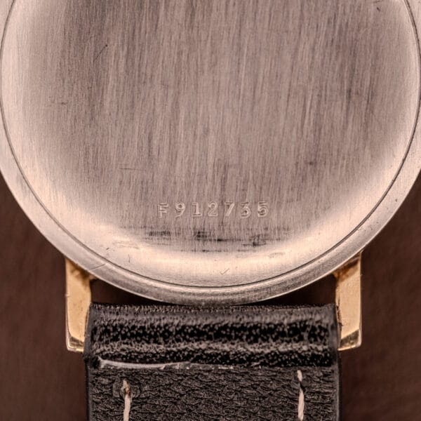 Close-up of a Bulova Manual Wind Date 10K RGP Cal. 11ALD c.1968 watch case back showing serial F912735 above a black leather strap, with 10K RGP and Cal. 11ALD markings visible.