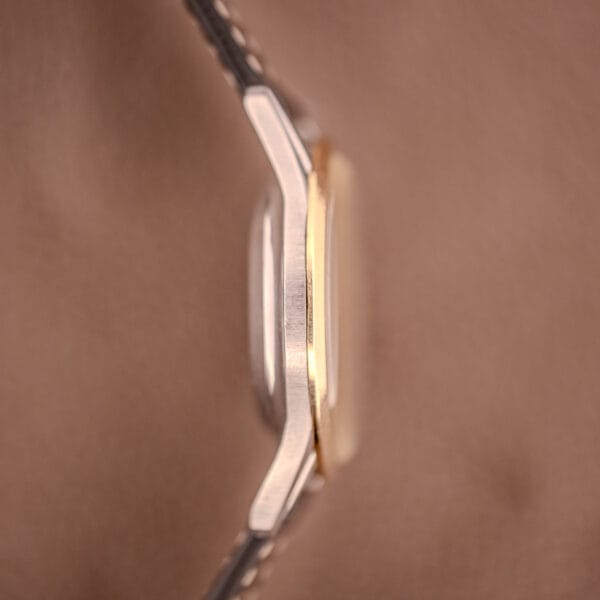 Close-up side view of a Bulova 30 Jewels Selfwinding Unishell Case 10K GF Bezel Cal. 10BZAC c.1961 wristwatch with gold accents, set against a blurred brown background.