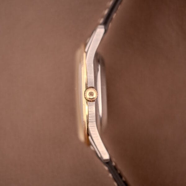 Side view of the Bulova 30 Jewels Selfwinding Unishell Case 10K GF Bezel Cal. 10BZAC c.1961 wristwatch crown and case, showcasing its selfwinding movement against a soft brown background.