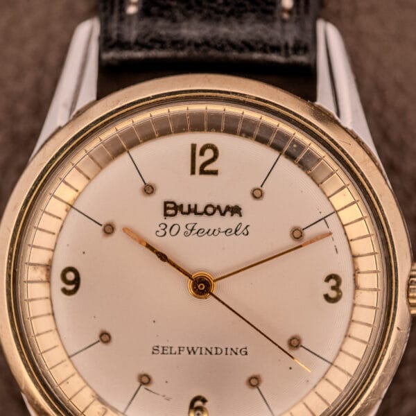 Close-up of a vintage Bulova 30 Jewels Selfwinding Unishell Case wristwatch (10K GF Bezel, Cal. 10BZAC, c.1961) with gold accents and black leather strap, dial marked "30 Jewels Selfwinding," showing the time 7:19:21.