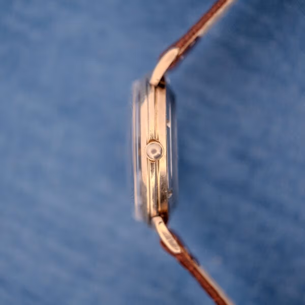 Side profile of the slim Cyma case showing gold-tone finish, polished crown at three, and curved lug.