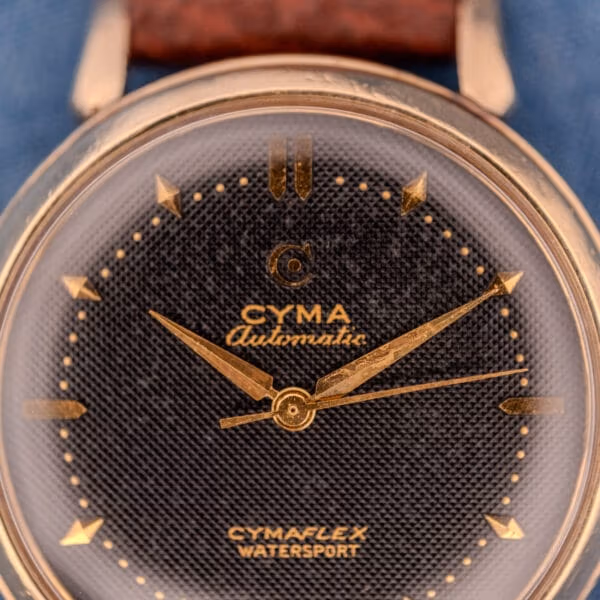 Macro close-up of the Cyma Cymaflex Watersport black waffle dial, gold dauphine hands and applied dart markers.