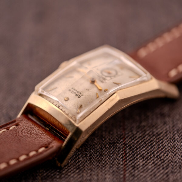 Close-up of a Gruen Curvex Precision "Pyramid Crystal" 10K GF Ref. 370-601 wristwatch with a brown leather strap, resting on a textured fabric surface.