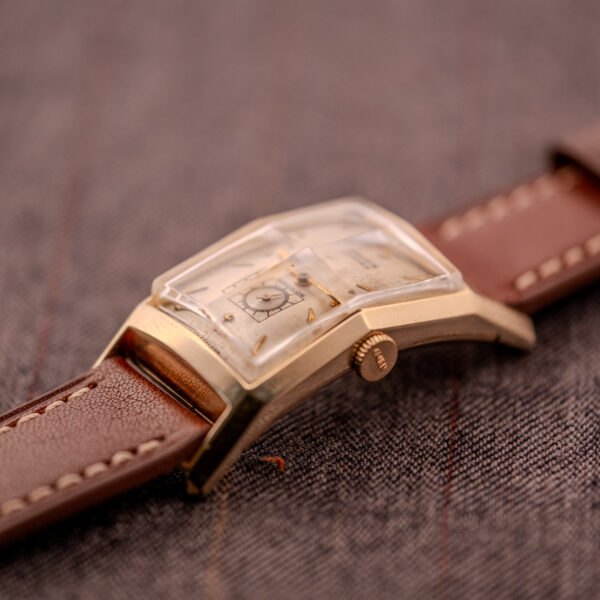 Close-up of a Gruen Curvex Precision "Pyramid Crystal" 10K GF Ref. 370-601 with a brown leather strap, set on textured fabric.