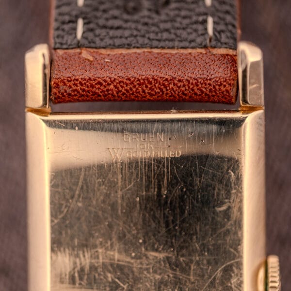 Close-up of a Gruen Curvex Precision "Pyramid Crystal" 10K GF Ref. 370-601 watch case back with visible scratches and a brown leather strap.