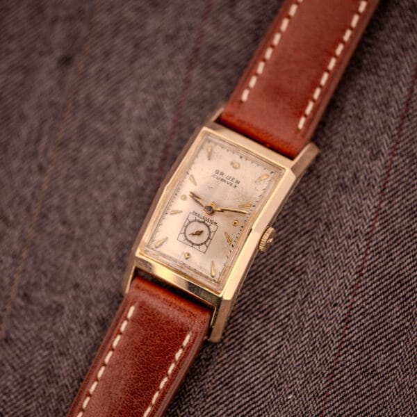 Gruen Curvex Precision "Pyramid Crystal" 10K GF Ref. 370-601 wristwatch with brown leather strap, displayed on gray herringbone fabric.