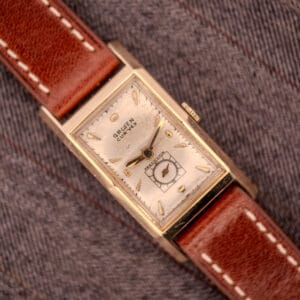 Gruen Curvex Precision "Pyramid Crystal" 10K GF Ref. 370-601 rectangular vintage watch with brown leather strap, displayed on gray fabric.
