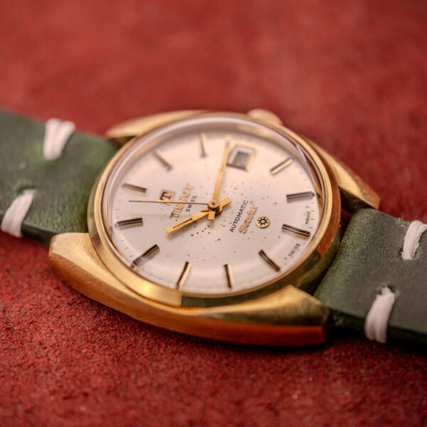 A Tissot Seastar Automatic Date Ref. 44660 Cal. 786-2 c.1970s with a gold case and green leather strap rests on a textured red surface.