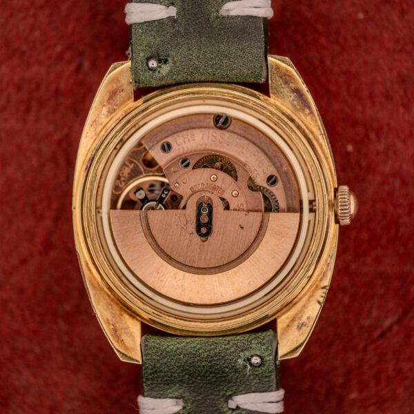 Close-up of a Tissot Seastar Automatic Date Ref. 44660 Cal. 786-2 c.1970s watch movement with a green strap and gold case on a red background.