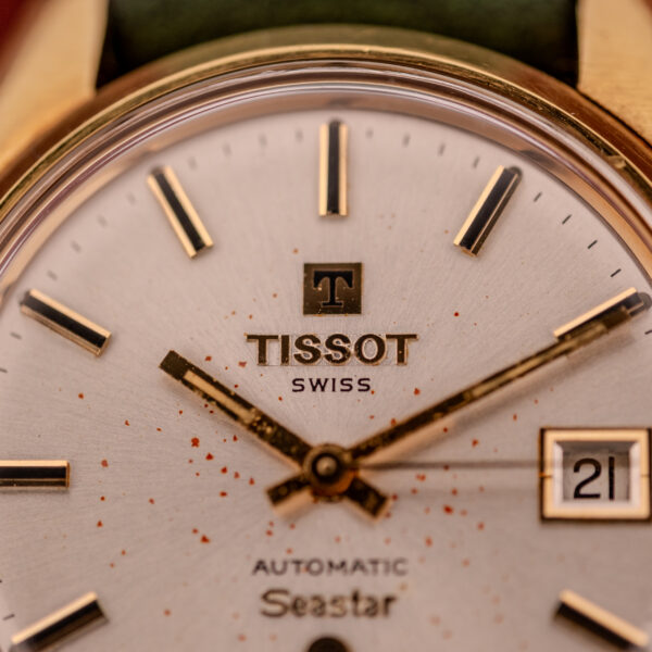 Close-up of a Tissot Seastar Automatic Date Ref. 44660 Cal. 786-2 c.1970s watch face, showing gold hands, date window at 3 o'clock, and small red spots.