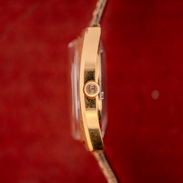 Side view of a Bulova Automatic Ambassador Day-Date Ref. 7532-1 Cal. 11AOACB c.1970s gold watch with a brown strap, set against a red background.