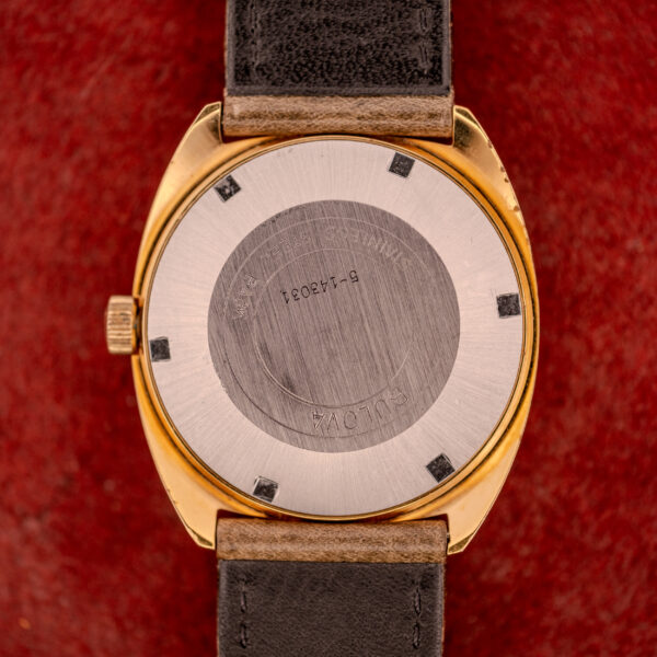 Close-up of the back of a Bulova Automatic Ambassador Day-Date Ref. 7532-1 (Cal. 11AOACB, c.1970s) gold wristwatch with leather strap, shown against a striking red background.