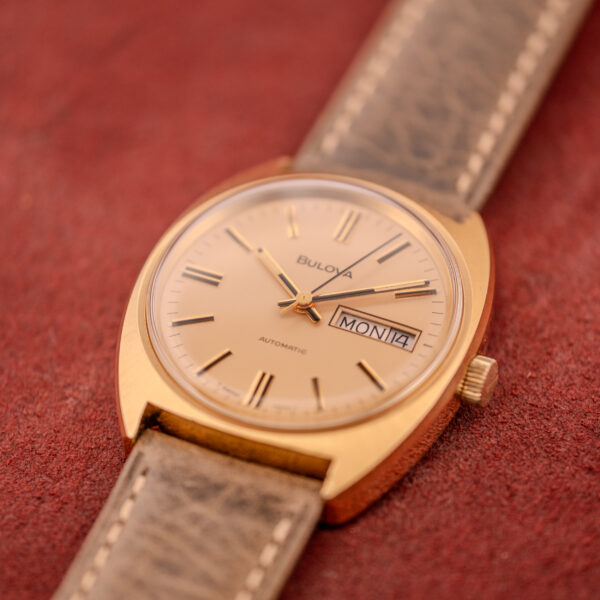 Bulova Automatic Ambassador Day-Date Ref. 7532-1, c.1970s, Cal. 11AOACB wristwatch with leather strap and day-date display on a red textured surface.