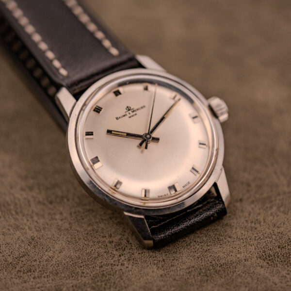 A Baume & Mercier Compressor Manual Wind Ref. 1193 Cal. 391 c.1967 wristwatch with a black leather strap rests on a brown textured surface.