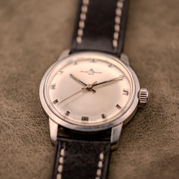 A Baume & Mercier Compressor Manual Wind Ref. 1193 Cal. 391 c.1967 wristwatch with a black leather strap is displayed on a textured surface.