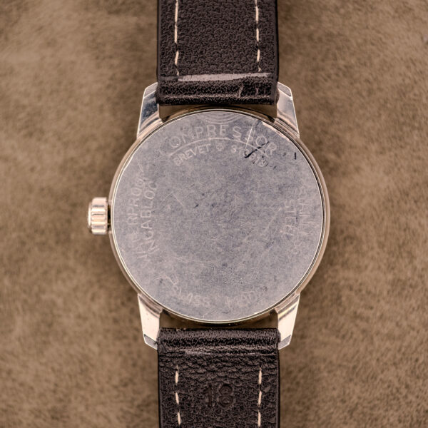 Close-up of the Baume & Mercier Compressor Manual Wind Ref. 1193 Cal. 391 c.1967, showcasing its brown leather strap and caseback detail as it rests on a tan surface.